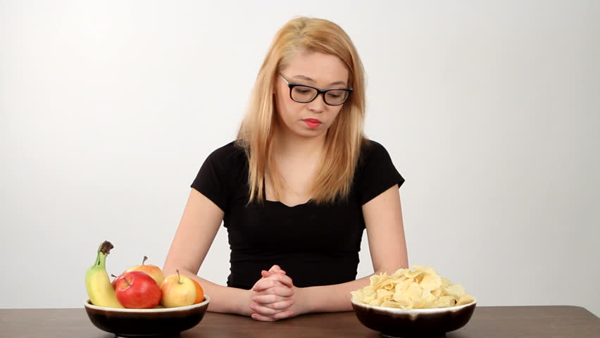 Teenager contemplates the choice of eating either some potato chips, junk food, or fruit, nutritious food, and chooses an apple.