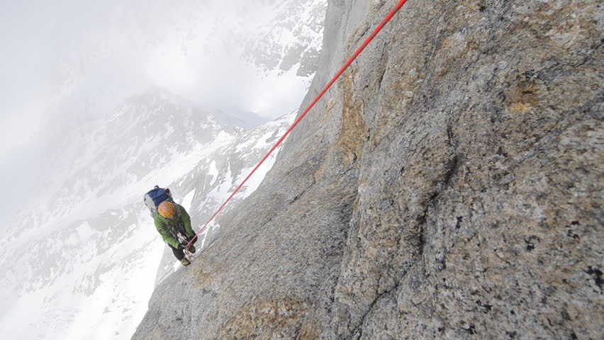 A mountain climber climbs up the side of a rock face in the cold, bright, snow covered Alaskan wilderness