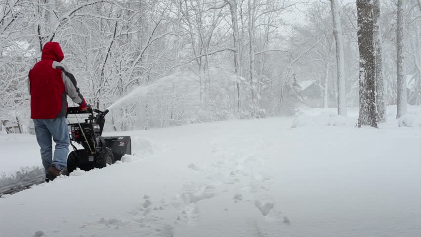 Worker pushing snow thrower during winter blizzard snowfall in residential area