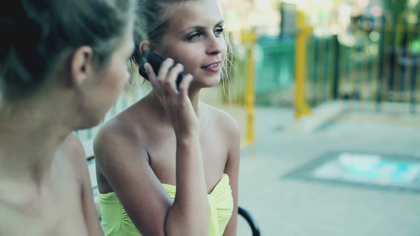 Female friends sitting on the bench and talking on cellphone, steadycam shot
