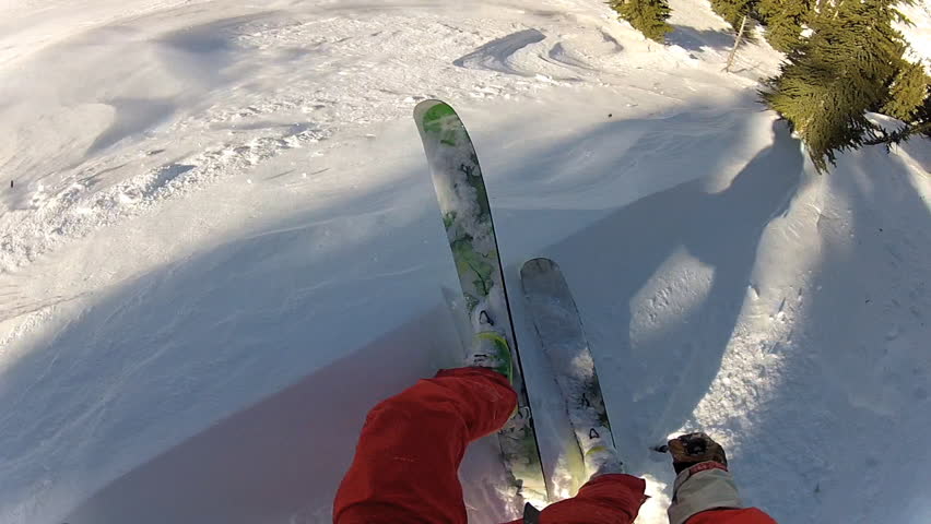 A skier carves back and forth as he rides down a mountain covered in fresh powder during the day. It is shot with a camera mounted to the athletes head and provides a POV, point of view, perspective.