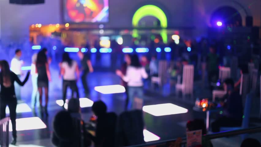 People dance at party in night club with color light, defocused