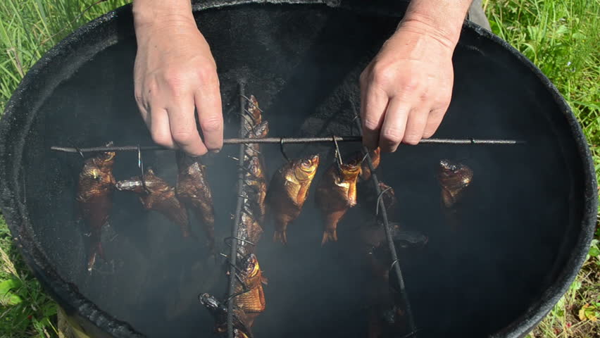 hand take smoked fish hang on shank in smokehouse. delicacy gourmet food.