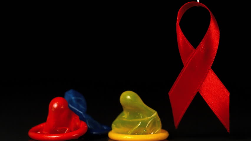 Coloured condoms dropping down beside red ribbon in slow motion