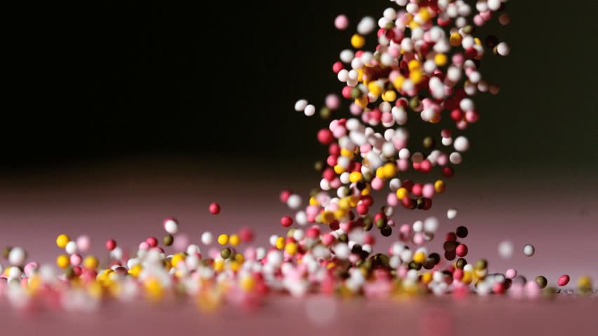 Sprinkles pouring onto pink surface on black background in slow motion