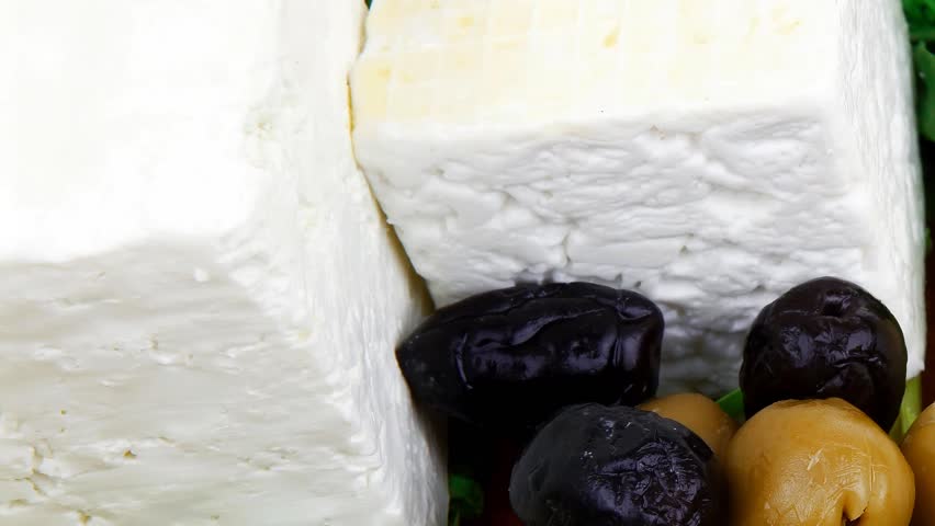 dairy food : feta white cheese cubes and round served on wooden cut plate with green leaves and olive oil isolated over white background