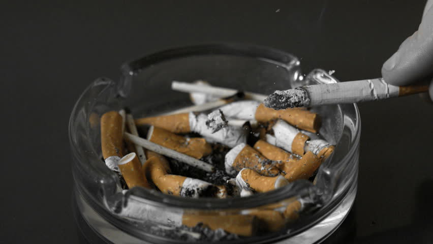 Hand tipping ash from cigarette into ashtray in slow motion