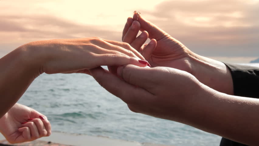Man placing engagement ring on female finger.