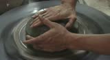 Two hands are molding clay into a vase.