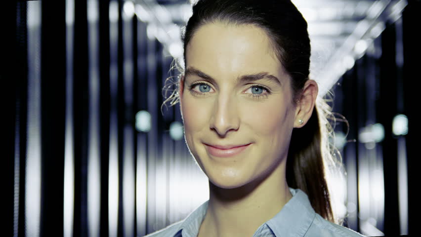 Portrait of a female IT engineer who is working in a data center with rows of server racks and computers. 