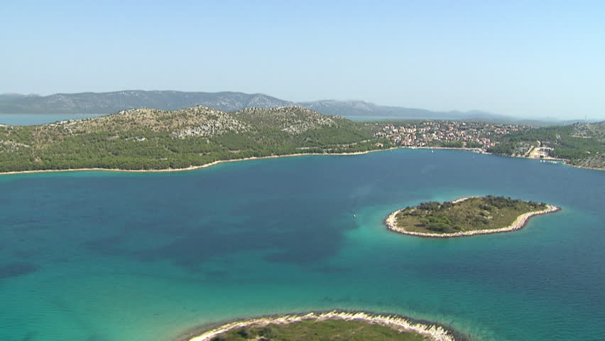 Flying over Adriatic sea and a small island in front of a big island. Aerial helicopter shot.