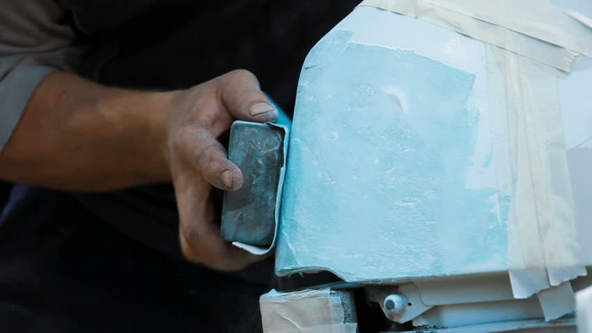 Close-up: a man is polishing damaged car surface with rasp for smearing putty on it.