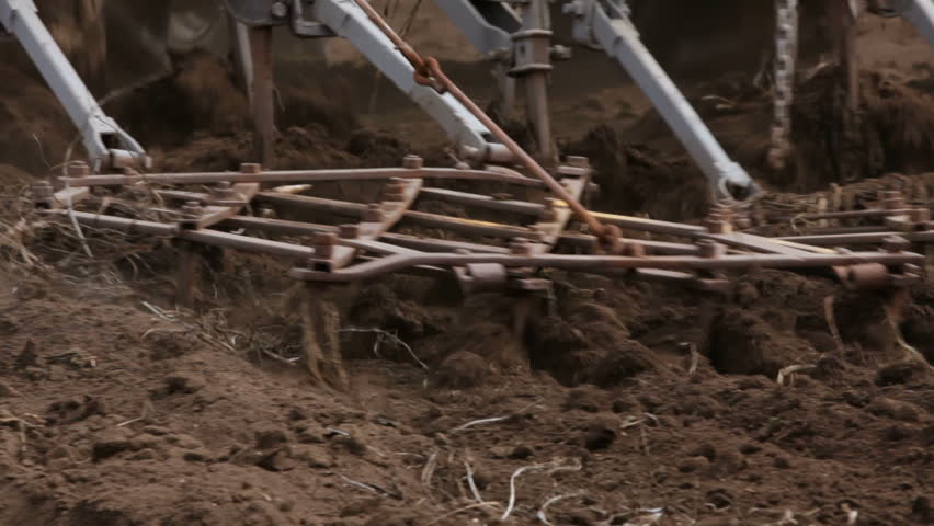 Closeup shot of tractor plows moving on the land while cultivating it.