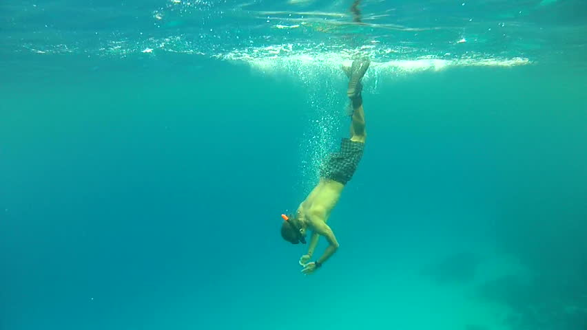 Man snorkeler dives into depth in the sea and tries to catch bubbles
