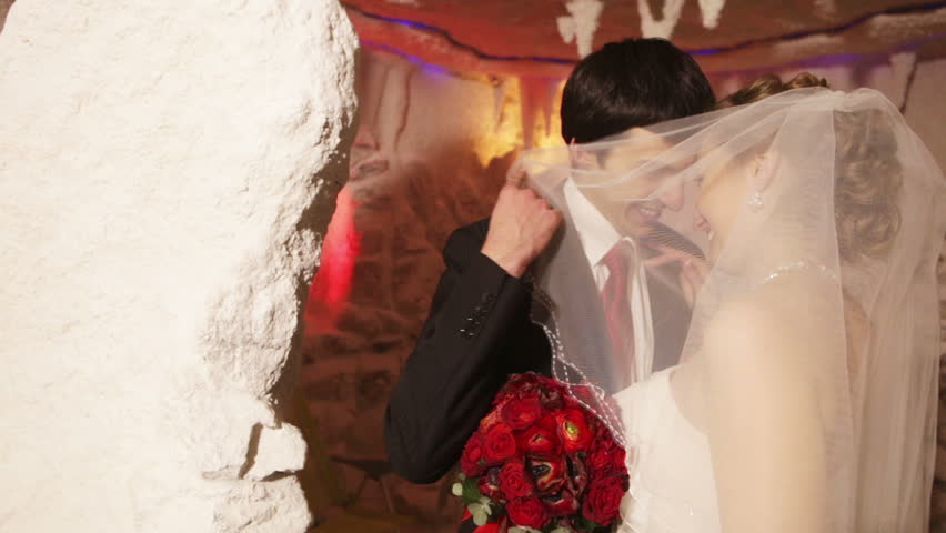 Young couple kissing hiding behind a veil in therapeutic salt cave.