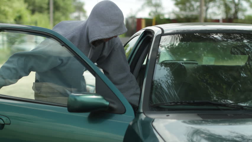 Burglar uses a "slim jim" to open up a car and steal a bag with a laptop computer. Recorded with camera on dolly.