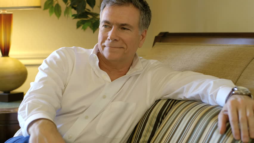 A handsome mature man relaxes in his living room contemplating pleasant thoughts revealed by a smile.