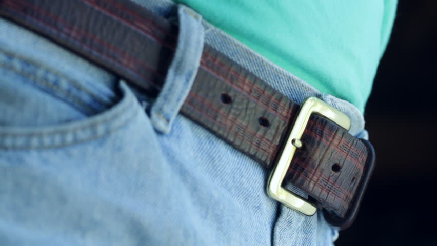 Pulling a brown leather belt tight on a pair of blue denim jeans. Shot with a macro lens and shallow depth of field.
