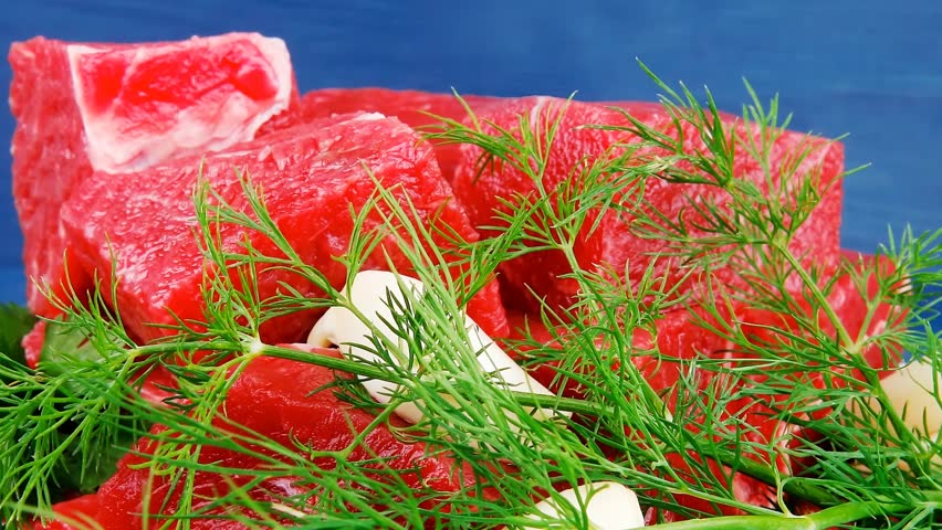 slices of raw fresh beef meat fillet in a white bowls with dill and green peppers serving over blue wooden table