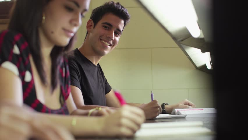 Happy student studying and writing, portrait of hispanic young man doing homework in college library and smiling at camera