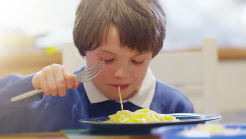 Close up of a very cute little boy who is having fun chewing and slurping his way through a steaming hot plate of spaghetti pasta.