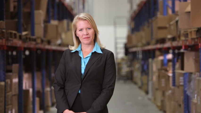 Female manager stands between shelves looking at camera before smiling and crossing arms. Shot on Canon 5d Mk2 with a frame rate of 30fps