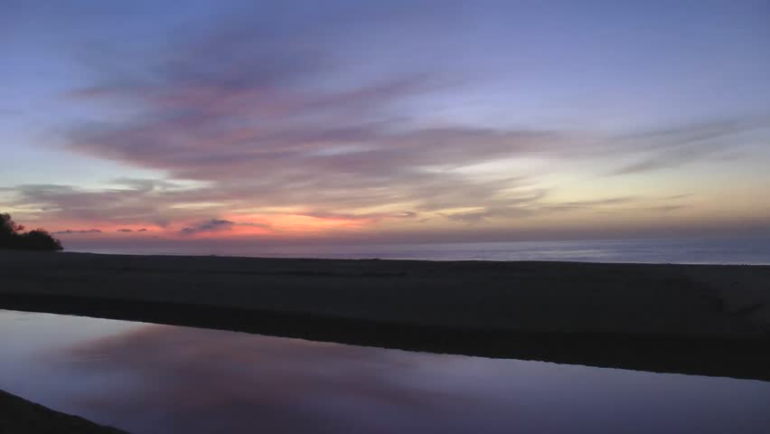 Sunrise bright and colorful through the beach and reflexing in the river.