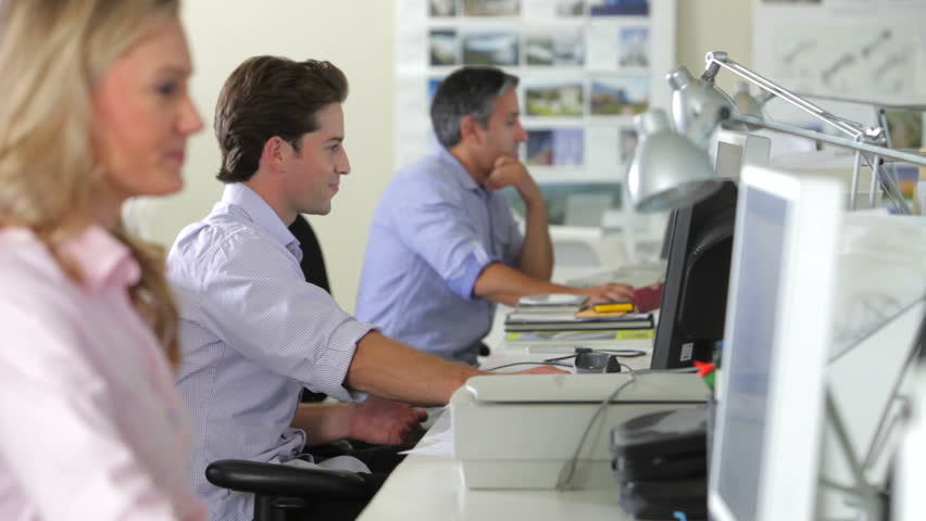 Businessman comes and sits on desk of younger male colleague and they discuss display on computer. Shot on Canon 5d Mk2 with a frame rate of 30fps