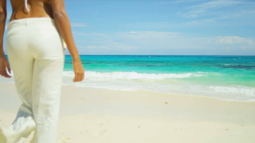 Young girl in bikini top trousers walking alone by ocean on remote island beach shot on RED EPIC