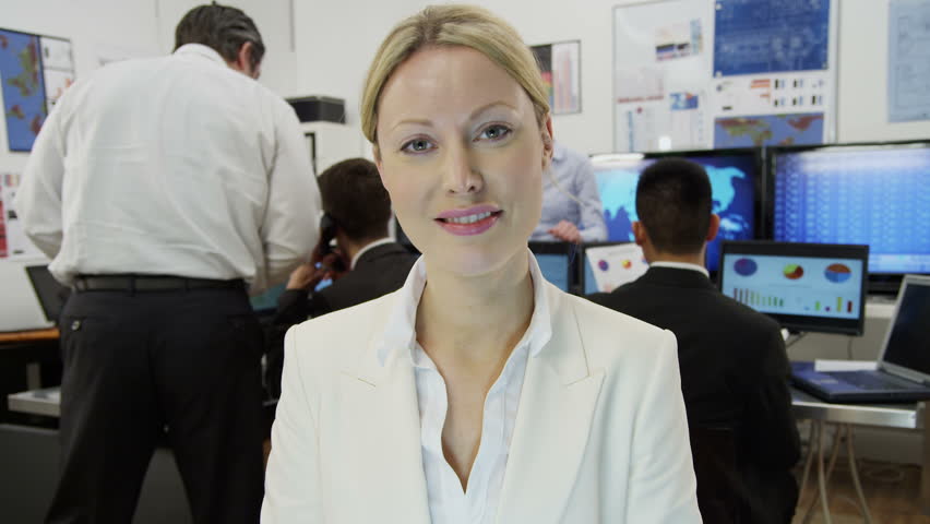 A beautiful young businesswoman is engaged in a video call with a client, as seen from the pov of the computer screen. She is sitting at her desk in a busy office filled with computers. 
