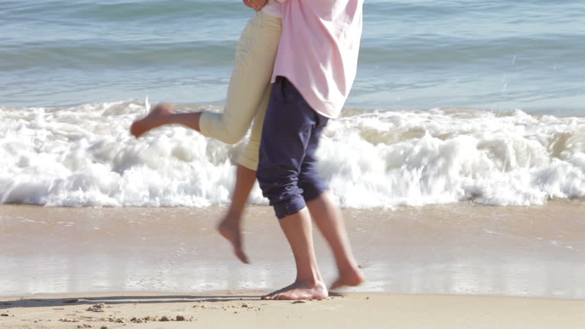 Man holds woman in the air as waves break behind them. Shot on Canon 5d Mk2 with a frame rate of 30fps