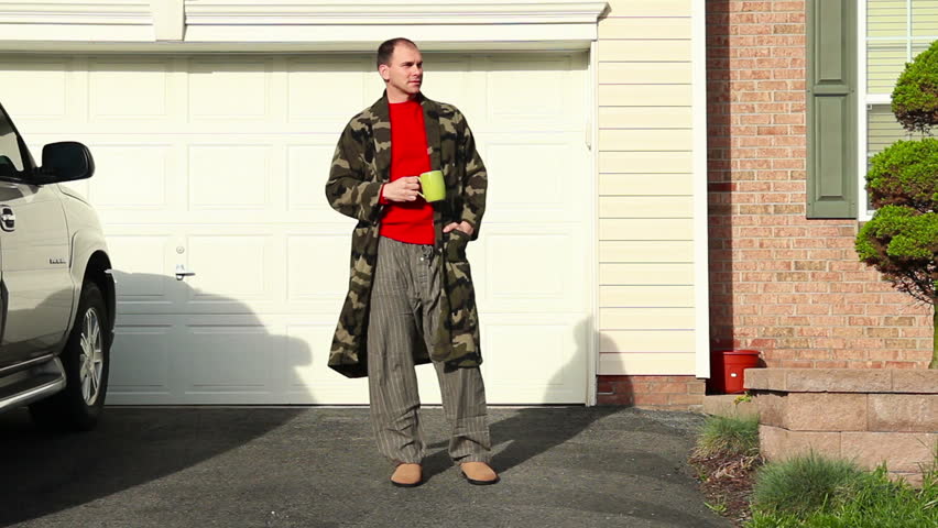 A man in his robe awaits for his daily paper on the driveway.