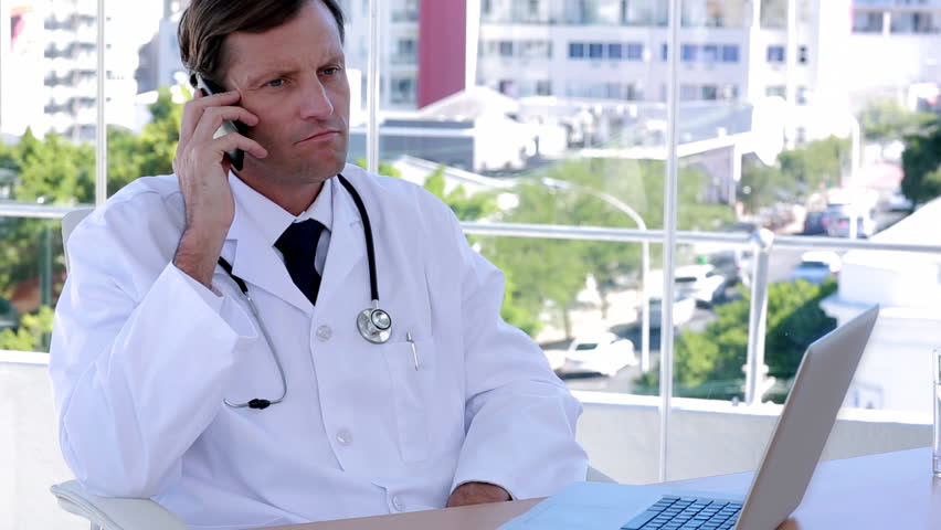 Doctor working on the phone and laptop at desk in office