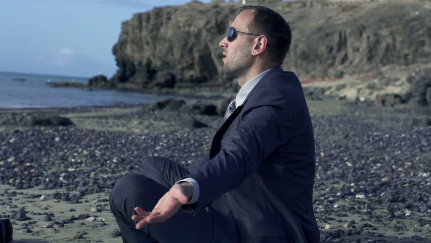 Businessman meditating on a sunny beach in the morning, slow motion shot at 60fps 
