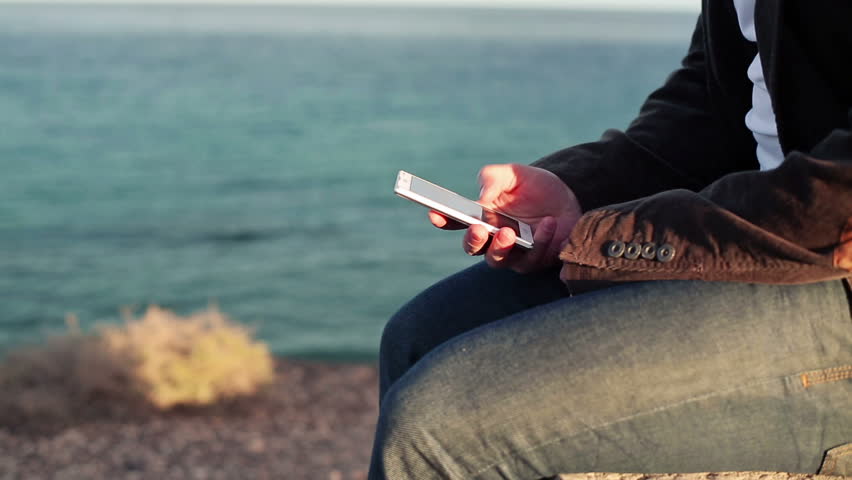Close up of man`s hands using smartphone by the sea
