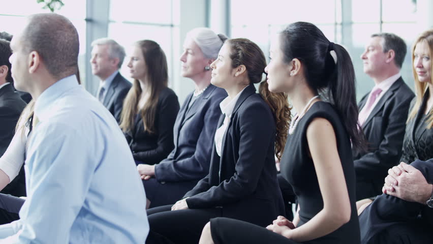 A multi ethnic group of business people of mixed ages are listening to a presentation at a business seminar and asking questions. 
