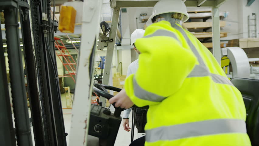 A female forklift truck driver arrives on shift in a factory or warehouse to take over from her male co-worker.