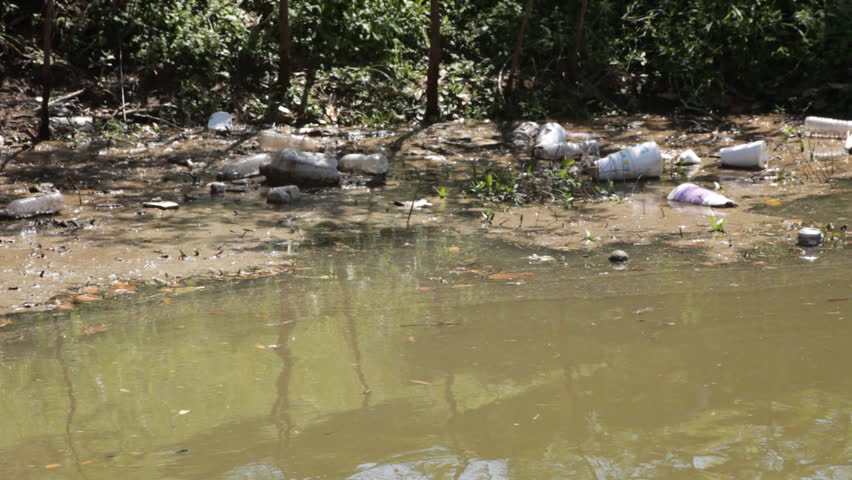 Trash from runoff litters the grassy area at the edge of a large drainage culvert.