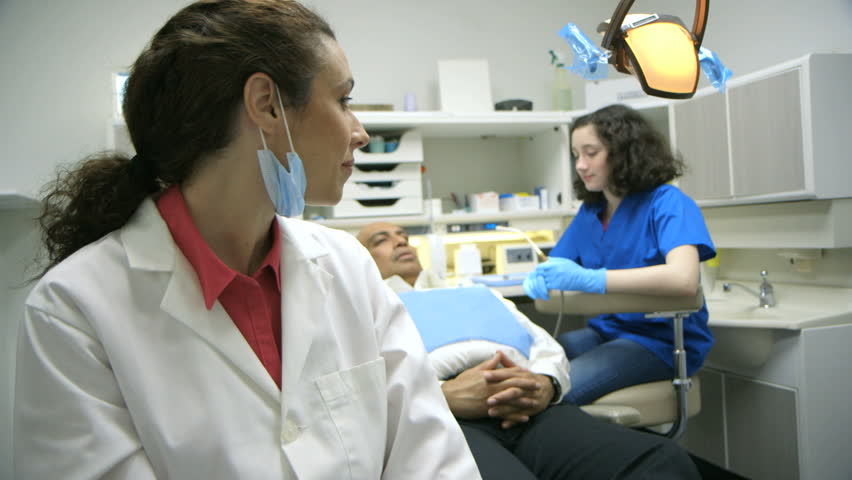 A dentist turns from listening to the dental hygienist consult with a young patient and smiles for the camera.