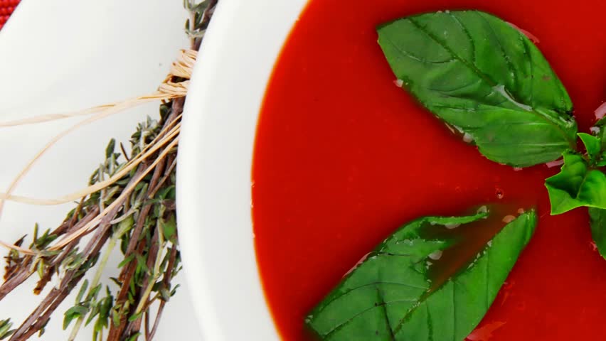 cold fresh diet tomato soup with basil thyme and dry pepper in big bowl over red mat on wood table ready to eat 1920x1080 intro motion slow hidef hd