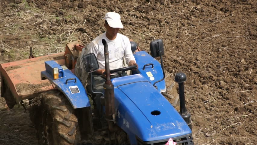 HEILONGJIANG PROVINCE, CHINA - CIRCA MAY 2013: Cat-skinner on the tractor with a plough. A male Chinese cat-skinner driving a small tractor. High angle, tracking continuos focus, close up.