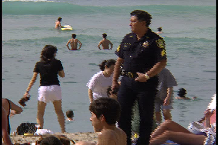 WAIKIKI BEACH, HONOLULU, HAWAII - JANUARY 30, 1997: Waikiki Beach, Hawaii; MS police officer on patrol walks between sunbathers on crowded beach. Ocean waves wash up on shore in background.
