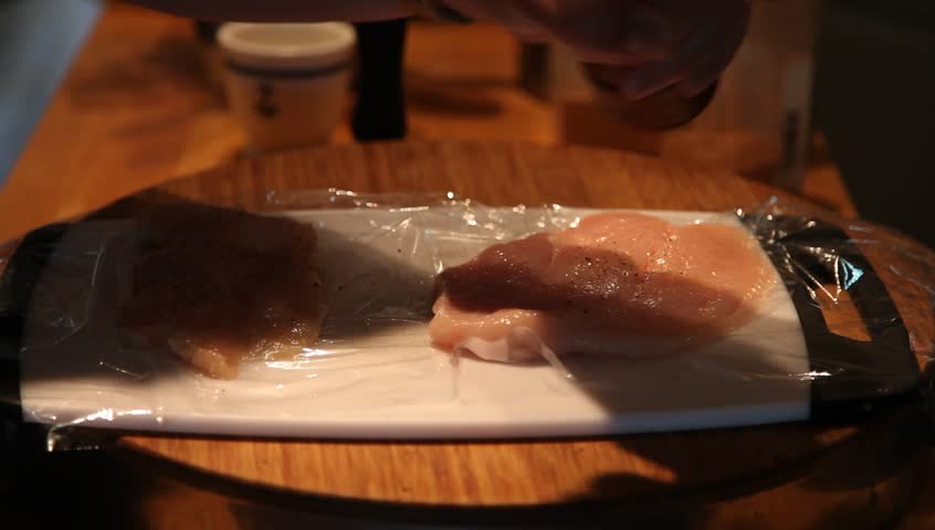Preparing chicken breasts for standard breading & pan frying by seasoning with salt & pepper from a pepper grinder
