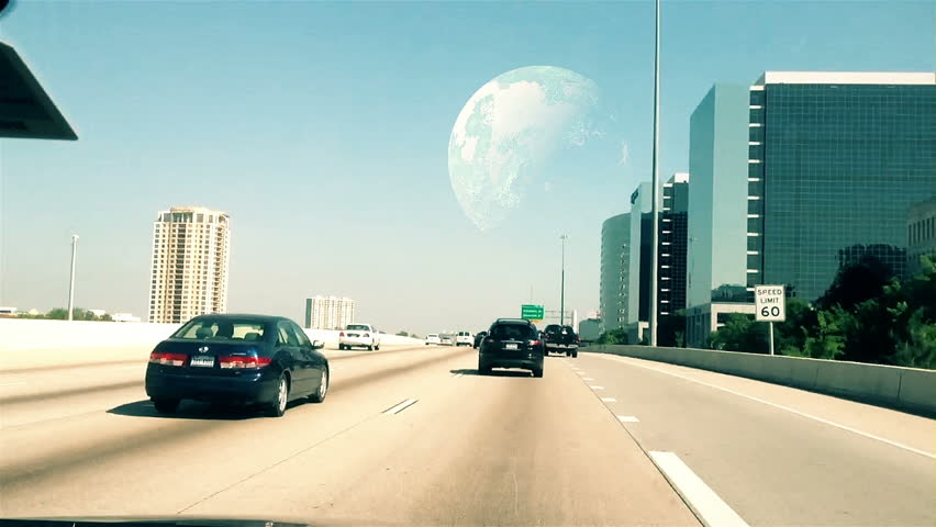 A large planet looms in the distance as seen through the windshield of a vehicle traveling down an interstate highway.