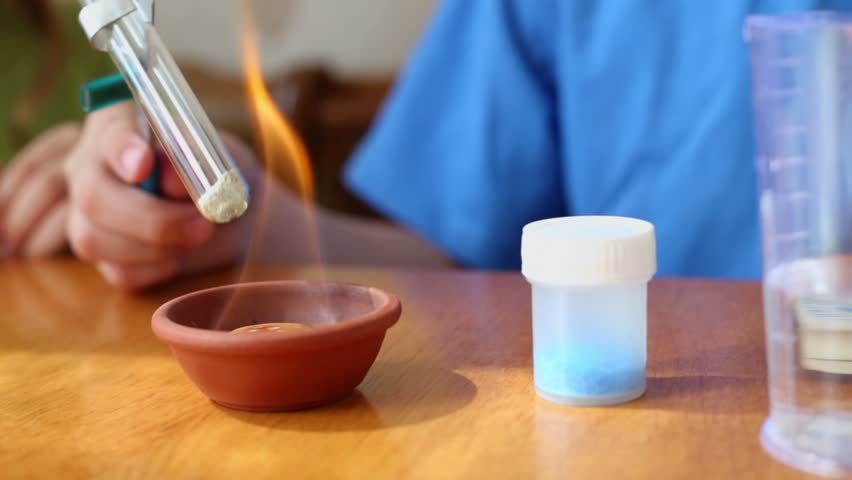 Young boy holds chemical tube above fire burner on table, closeup