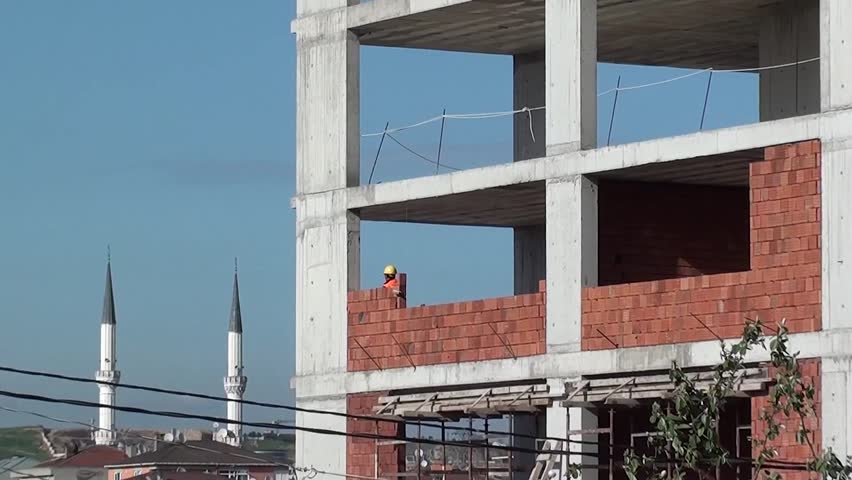 Bricklayer is at job, mosque is seen