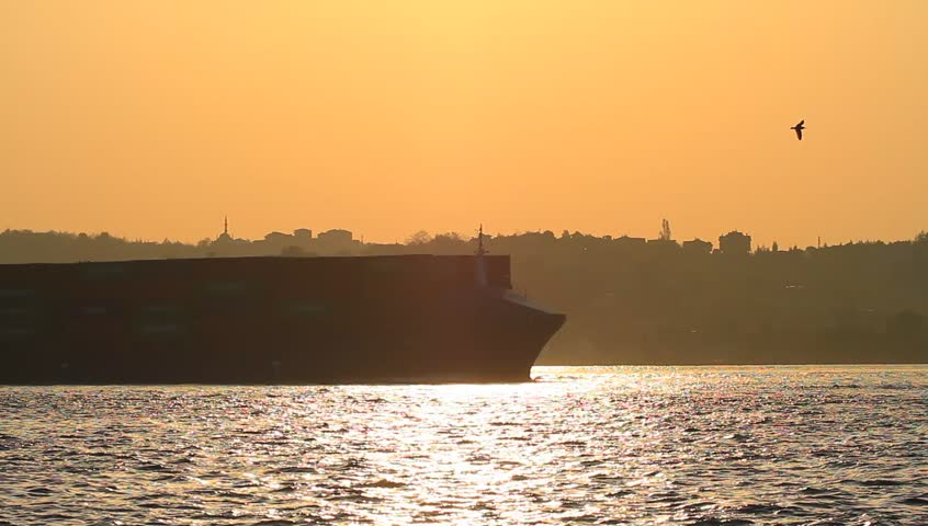 Large cargo ship sailing past the city in Istanbul, Turkey. Container ship cruising full of containers against sunset
