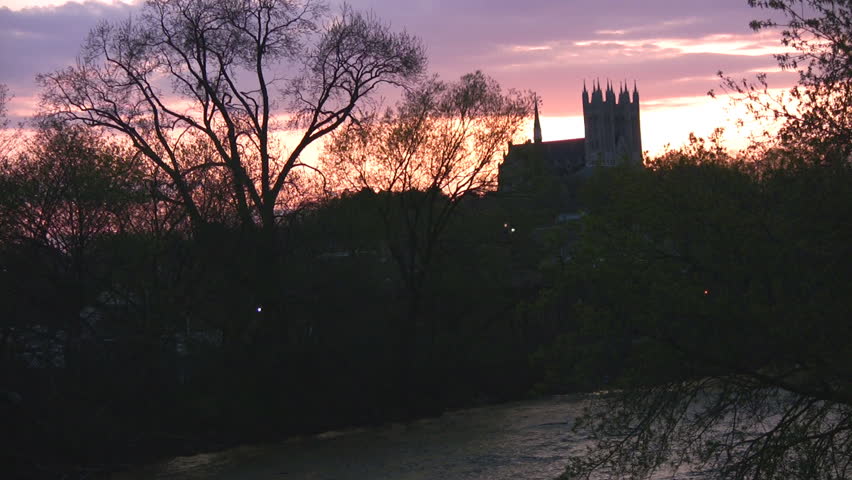 A church in the distance, highlighted by a sunset full of purples, oranges, and pinks, with a river below.  Guelph, Ontario, Canada