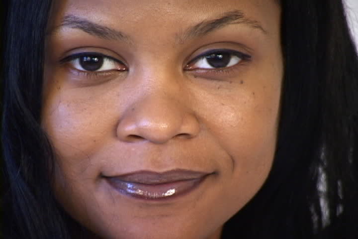 A young and happy African American business woman smiles at the camera. This closeup of the face was shot with fixed focus from a tripod with a miniDV camera. 