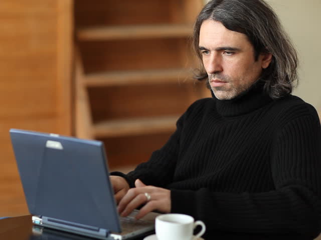 The man works on the computer and drinks coffee 